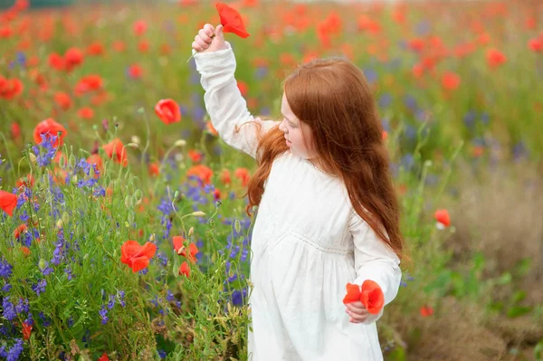 Czerwona głowa dziecko dziewczynka gra na polu z kwiatami. — Zdjęcie stockowe
