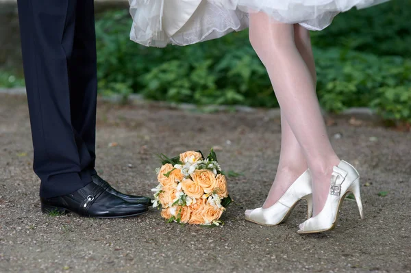 Closeup των ποδιών νύφης και του γαμπρού και γαμήλια ανθοδέσμη των λουλουδιών — Φωτογραφία Αρχείου