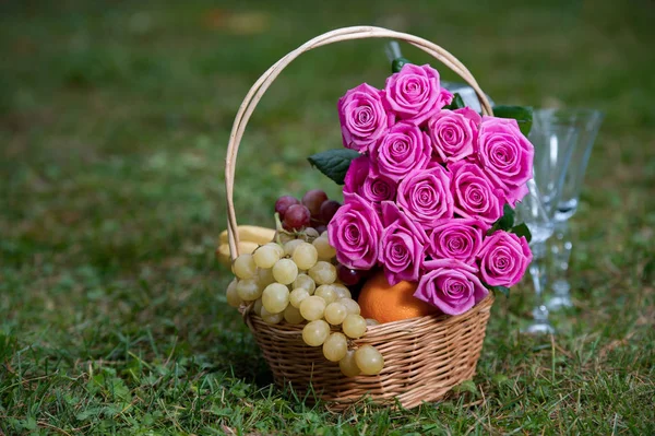 bouquet of pink roses with fresh fruit in a wicker basket on a g