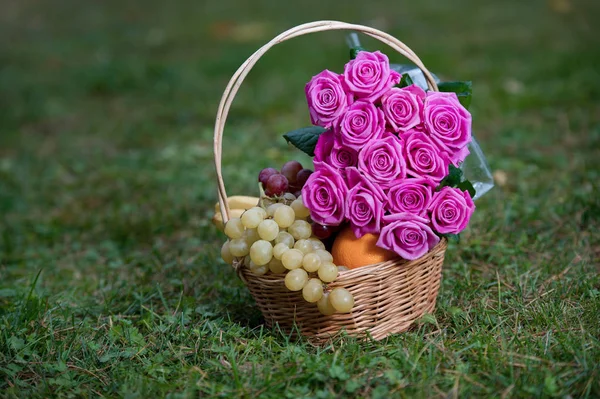 bouquet of pink roses and fruits in a basket on a grass