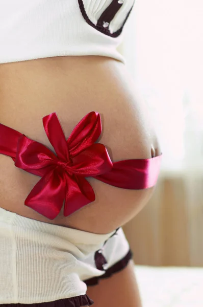 Barriga da mulher grávida com uma fita vermelha — Fotografia de Stock