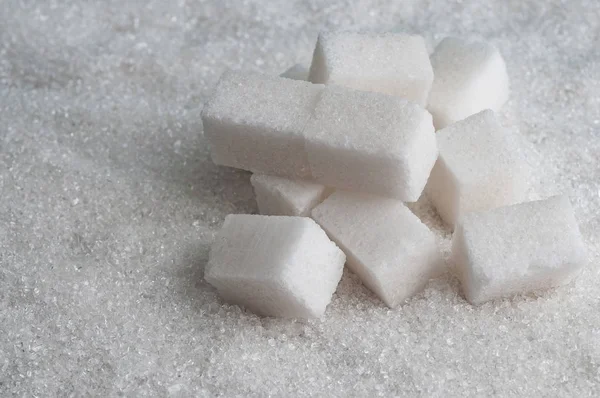 Cubos de azúcar sobre fondo de azúcar granulado blanco — Foto de Stock