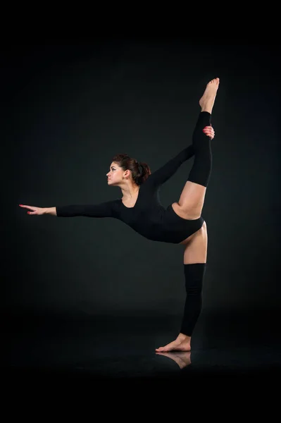 Menina de ioga esportiva no fundo preto fazendo exercícios de alongamento — Fotografia de Stock