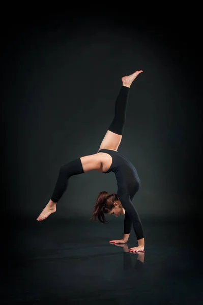 Красивая гибкая женщина делает акробатические элементы на черном фоне — стоковое фото