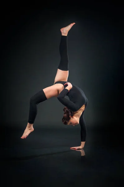 Beautiful flexible woman doing acrobatic elements against dark b — Stock Photo, Image