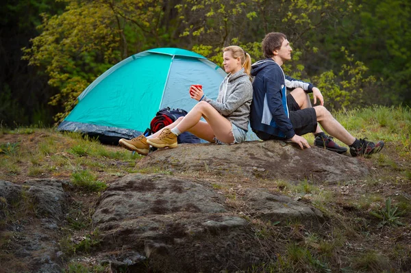 Couple hikers in the wild forest. Man and woman resting with cup of tea near the tent. Travel, vacation, holidays and adventure concept. Forest Mountain landscape background