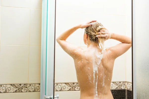 Vista posterior de la joven lavando su cuerpo en la ducha con champú —  Fotos de Stock