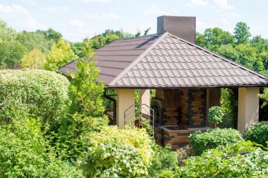 Gazebo with place for barbecue in a juicy green summer garden clipart