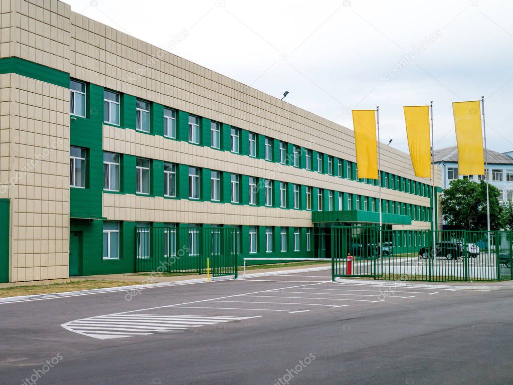 Photo of a modern green factory building, with parking lot