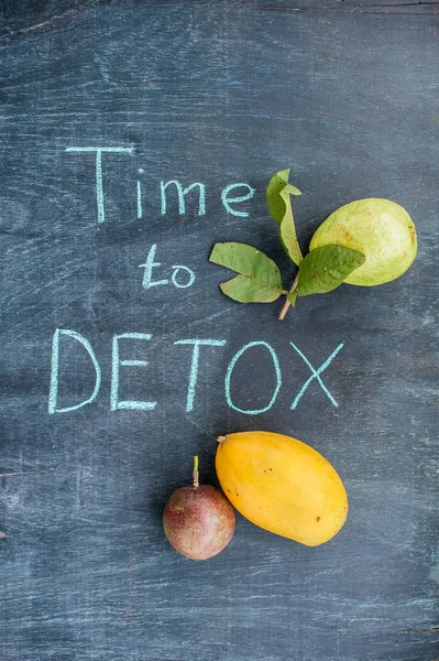 TIME TO DETOX chalk inscription on the wooden table fruits: mango, passion fruit and guava. Health Concept