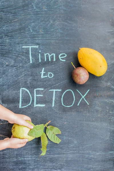 TIME TO DETOX chalk inscription on the wooden table fruits: mango, passion fruit and guava. Hand stretching  . Health Concept