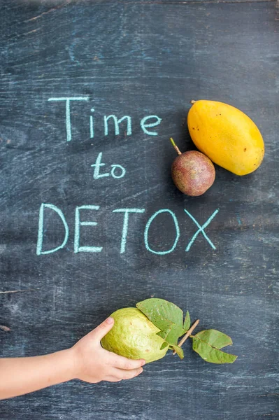 Tijd om de Detox krijt inscriptie op de houten tafel fruit: mango, passievrucht en guave. Hand die zich uitstrekt. Gezondheid Concept — Stockfoto