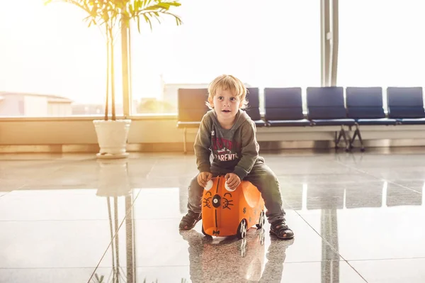 Netter kleiner Junge mit orangefarbenem Koffer am Flughafen — Stockfoto