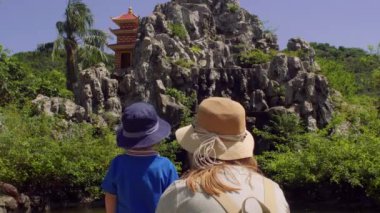 Anne ve oğlu makak maymunları kayaların üzerinde atlama bakıyor. Monkey Island, Vietnam