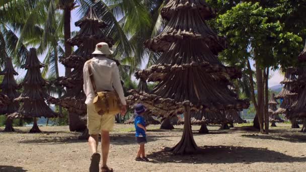 Padre e hijo sentados bajo árboles de navidad hechos de materiales reciclados de viejas ramas de palma — Vídeo de stock