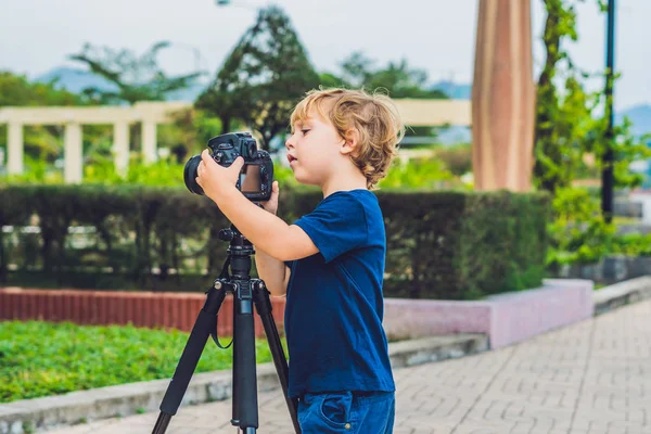 O menino da criança tira fotos em uma câmera em um tripé — Fotografia de Stock