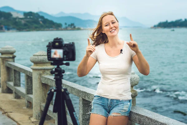A young woman blogger leads her video blog in front of a camera by the sea. Blogger concept — Stock Photo, Image