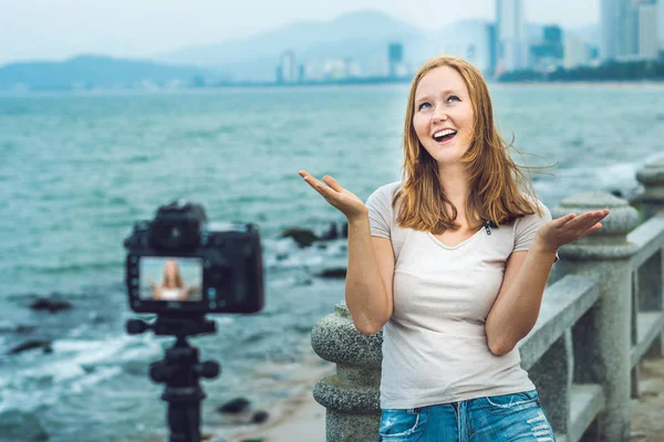 Uma jovem blogueira leva seu vídeo blog na frente de uma câmera à beira-mar. Conceito de blogueiro — Fotografia de Stock