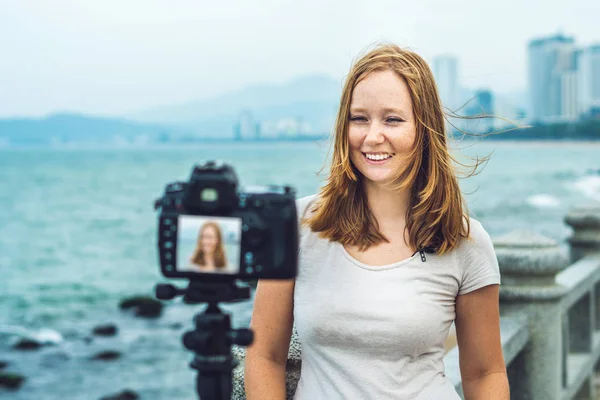 Uma jovem blogueira leva seu vídeo blog na frente de uma câmera à beira-mar. Conceito de blogueiro — Fotografia de Stock
