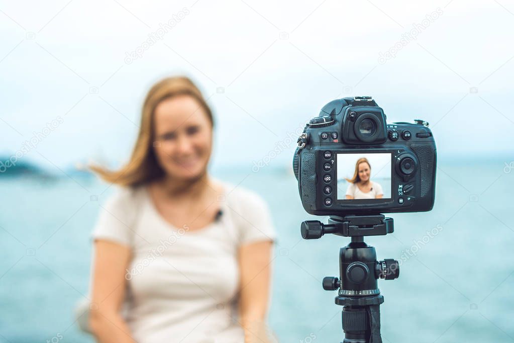 A young woman blogger leads her video blog in front of a camera by the sea. Blogger concept