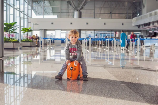 Netter kleiner Junge mit orangefarbenem Koffer am Flughafen — Stockfoto