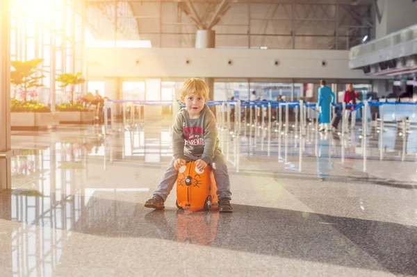 Ładny chłopczyk z walizce pomarańczowy na lotnisku — Zdjęcie stockowe