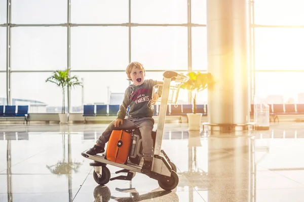 Netter kleiner Junge mit orangefarbenem Koffer am Flughafen. der Junge auf dem Trolley und der Flughafen — Stockfoto