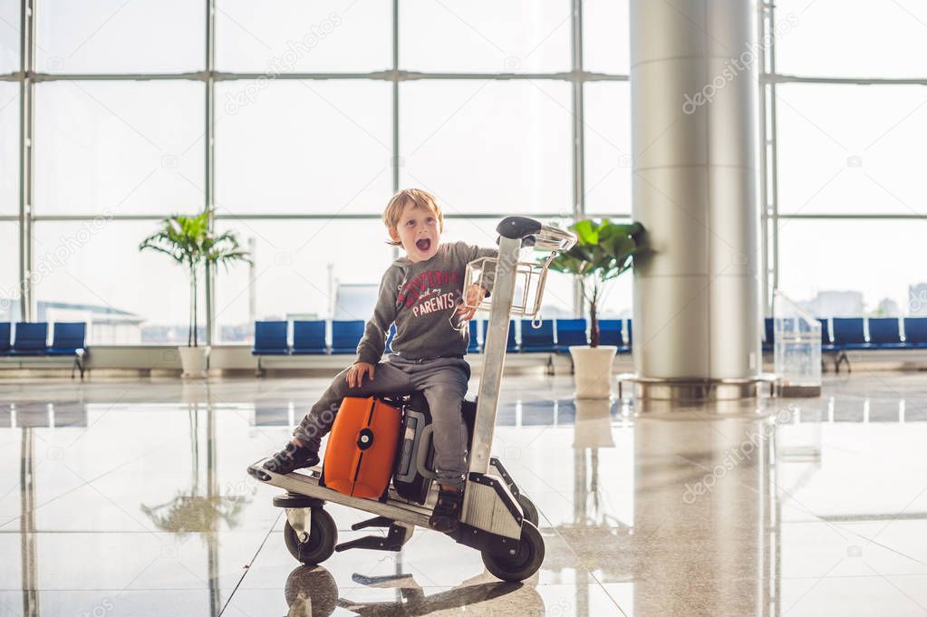 Cute little boy with orange suitcase at airport. The boy on the trolley and the airport