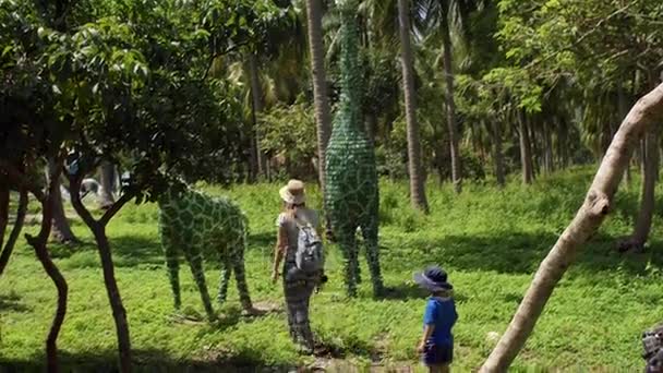 Moeder en zoon lopen door een tuin met een beelden van dieren van een gerecyclede flessen materialen gemaakt. Vietnam. — Stockvideo