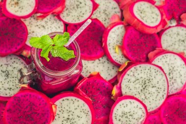 Eski bir ahşap zemin üzerinde dragon meyve parçaları ve kırmızı organik dragon meyve smoothies