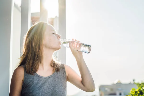 Mujer joven está bebiendo agua en el fondo del atardecer — Foto de Stock
