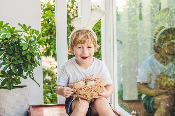 Un bambino carino con le orecchie da coniglietto il giorno di Pasqua. Ragazzo che tiene nido con uova — Foto Stock