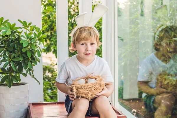 Lindo niño pequeño con orejas de conejo en el día de Pascua. Niño sosteniendo nido con huevos — Foto de Stock