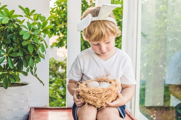 Χαριτωμένο μικρό αγόρι παιδί φορώντας bunny αυτιά την ημέρα του Πάσχα. Αγόρι που κατέχουν φωλιά με αυγά — Φωτογραφία Αρχείου