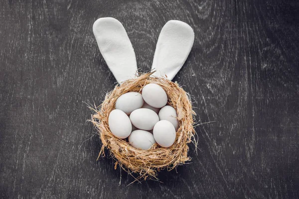 Un nido con tres huevos blancos de Pascua y orejas de conejo en casa el día de Pascua. Celebrando la Pascua en primavera. Pintura de huevos — Foto de Stock