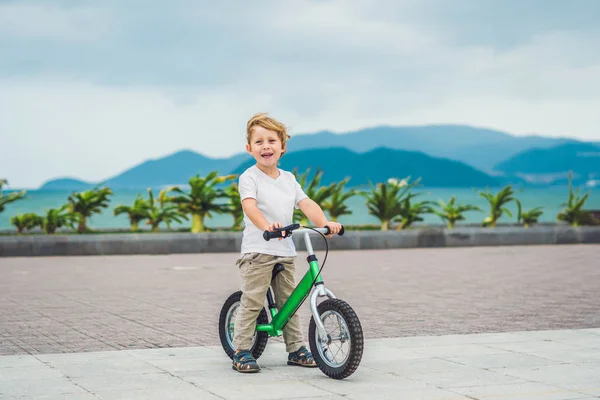 Aktiver blonder Junge und Fahrrad in der Nähe des Meeres. Kleinkind träumt und hat Spaß an warmen Sommertagen. Spiele im Freien für Kinder. Laufrad-Konzept — Stockfoto