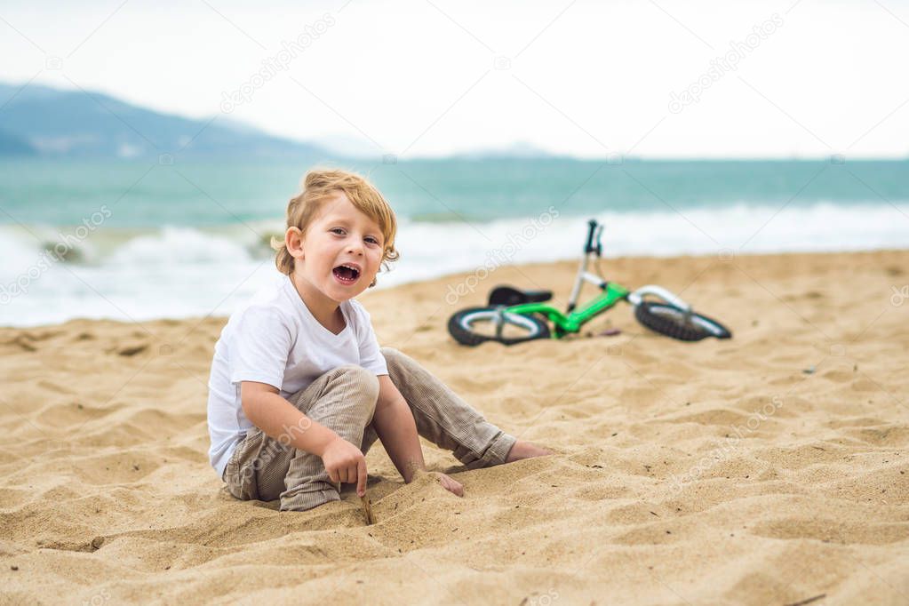Active blond kid boy and bicycle near the sea. Toddler child dreaming and having fun on warm summer day. outdoors games for children. Balance bike concept