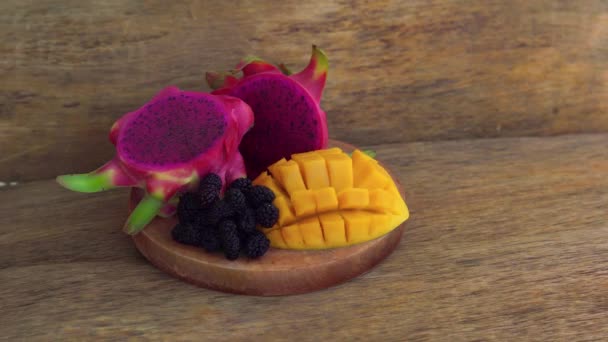 Vrouw zet een plaat met een gesneden dragon fruit en mango op een oude houten achtergrond — Stockvideo