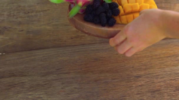 Женщина кладет тарелку с нарезанным фруктом дракона и манго на старом деревянном фоне — стоковое видео
