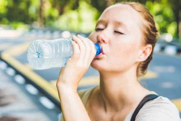 Mujer joven en el clima caliente bebe agua de una botella — Foto de Stock