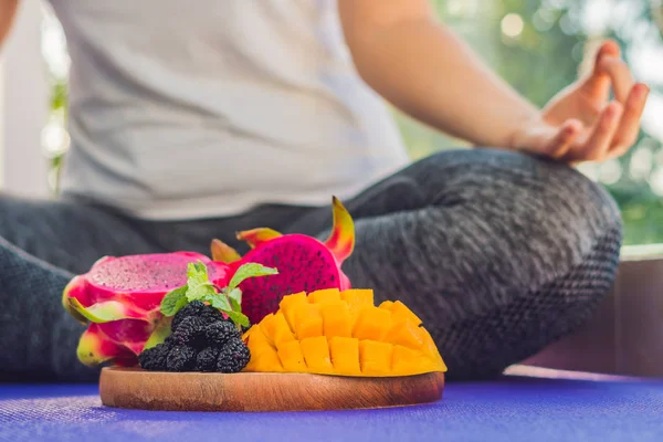 Mano de una mujer meditando en una pose de yoga, sentada en loto con frutas frente a su fruta de dragón, mango y morera —  Fotos de Stock