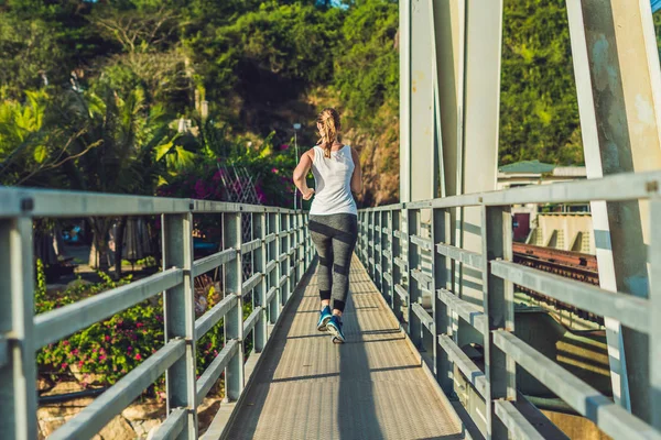 Красивая женщина бежит по мосту на закате — стоковое фото