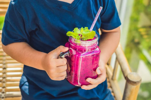 El niño sostiene batidos de una fruta de dragón con una hoja de menta y una pajita para beber. — Foto de Stock