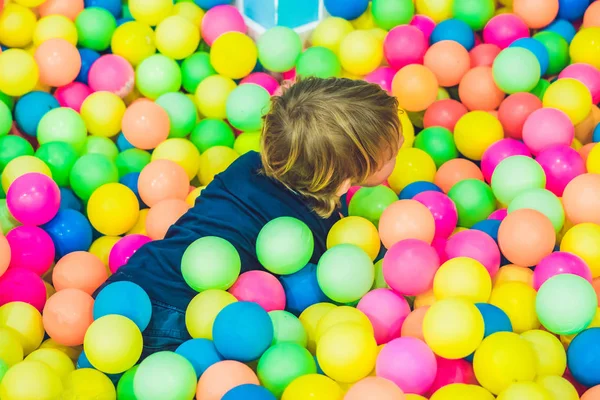 Niño niño feliz jugando en coloridas bolas de plástico patio vista alta. Divertido niño divirtiéndose en el interior —  Fotos de Stock