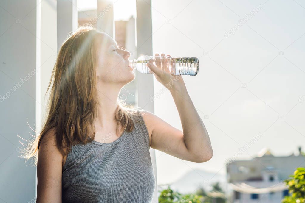 Young woman is drinking water on the sunset background