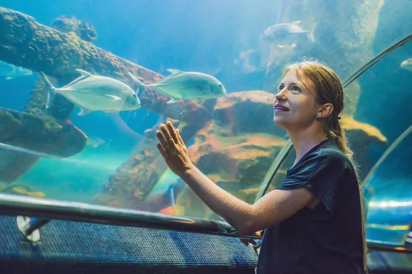 Giovane donna che guarda i pesci in un acquario tunnel — Foto Stock