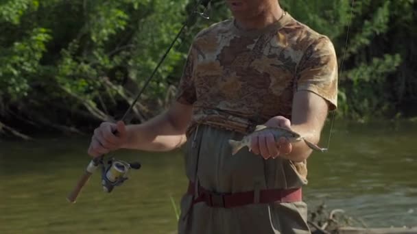 Pescador mostra à câmera um peixe que ele acabou de pegar com um curto ultraleve girando — Vídeo de Stock
