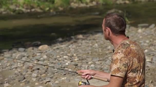 Primer plano de un hombre pescando en un río de montaña con un giro ultraligero usando wobblers de pesca — Vídeo de stock