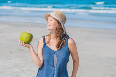 Genç kadın kumsalda Hindistan cevizi sütü içme.