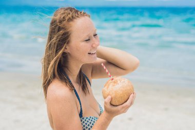 Genç kadın kumsalda Hindistan cevizi sütü içme.